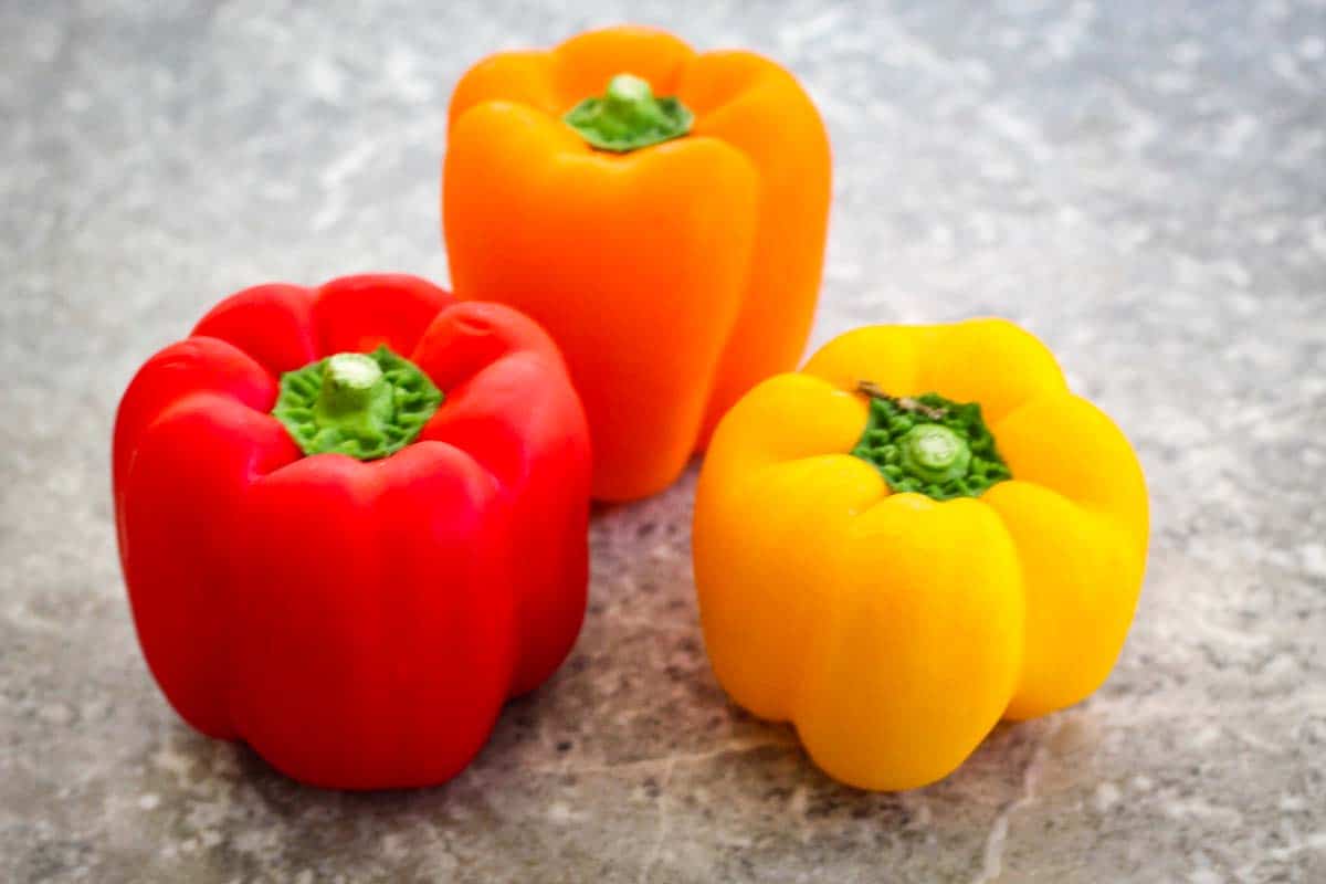Three bell peppers, red, yellow and orange next to each other. 