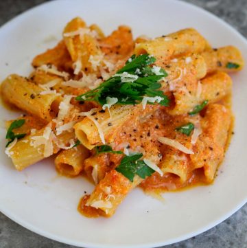 A plate of rigatoni pasta with an orange/reddish creamy sauce. Pasta is garnished with parsley and cheese.