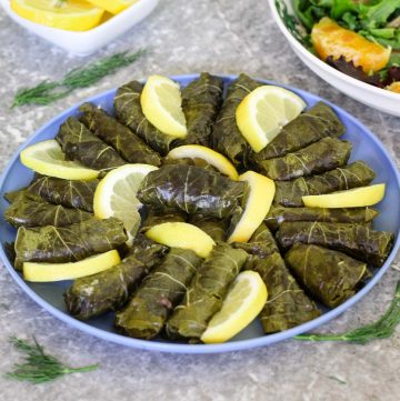 A blue, round platter with stuffed grape leaves and lots of lemon slices.