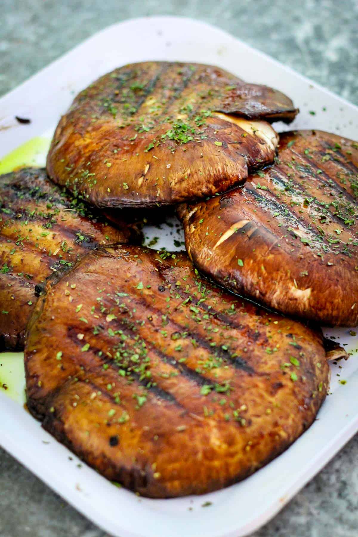 Four grilled portobello mushrooms on a platter. They look garnished with green herbs.