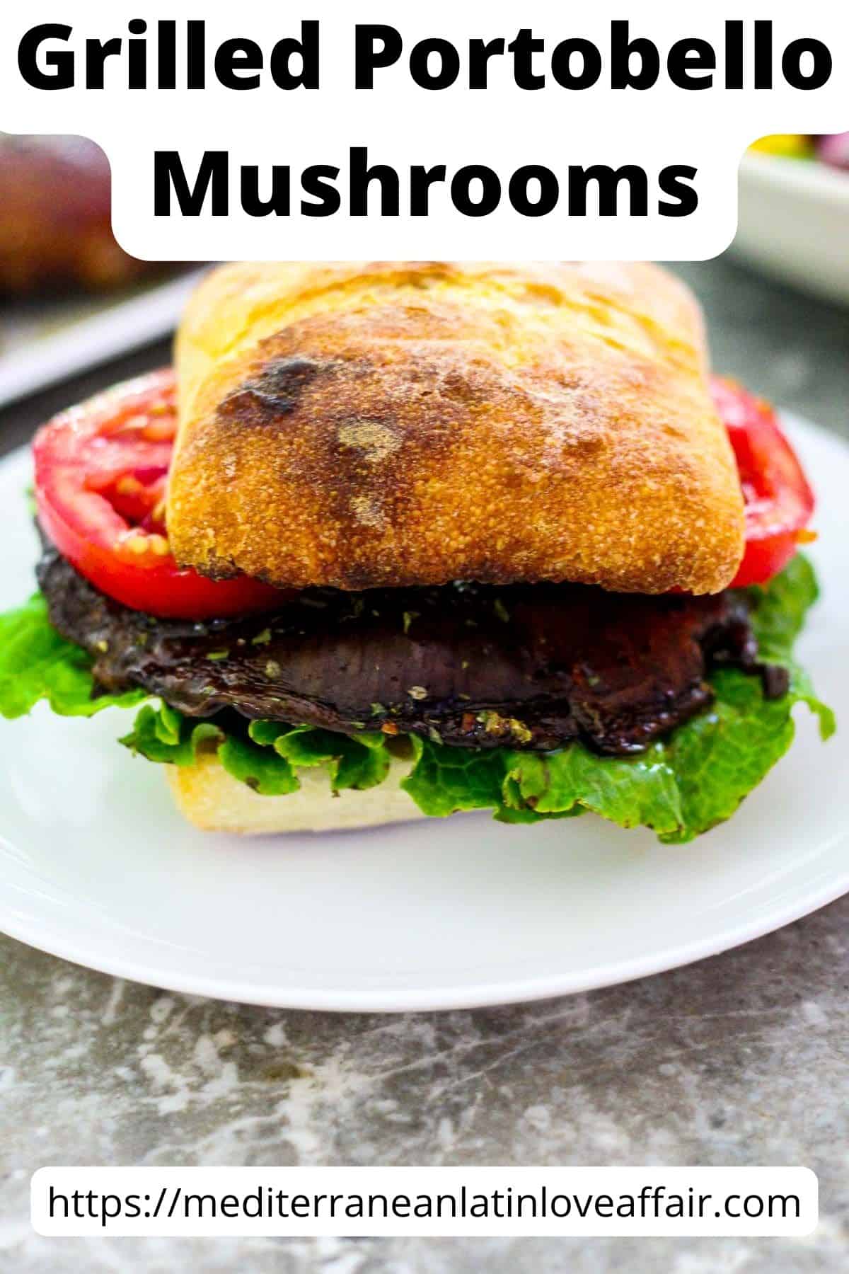 An image prepared for Pinterest. It shows a sandwich with grilled portobello mushrooms, tomatoes, lettuce on an artisanal roll. The image has a title bar that reads Grilled Portobello Mushrooms and a website link to the bottom. 