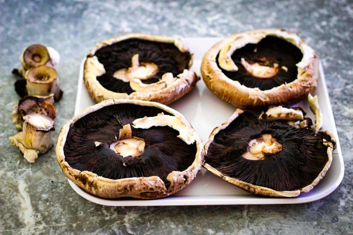 Portobello mushrooms stem side up. Next to the platter with mushrooms, you see the stems already removed on the side. 