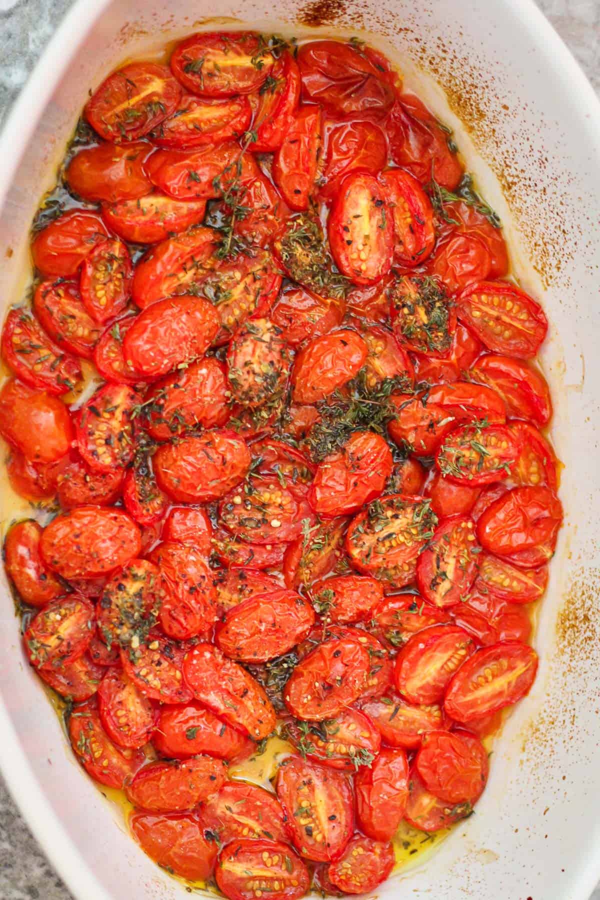 Roasted grape tomatoes, halved with lots of seasonings. Tomatoes are still in a baking tray.