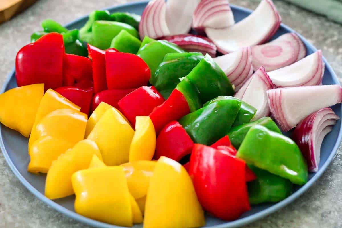 Yellow, red and green bell peppers plus a red onion all cut for kebabs and ready on a platter. 