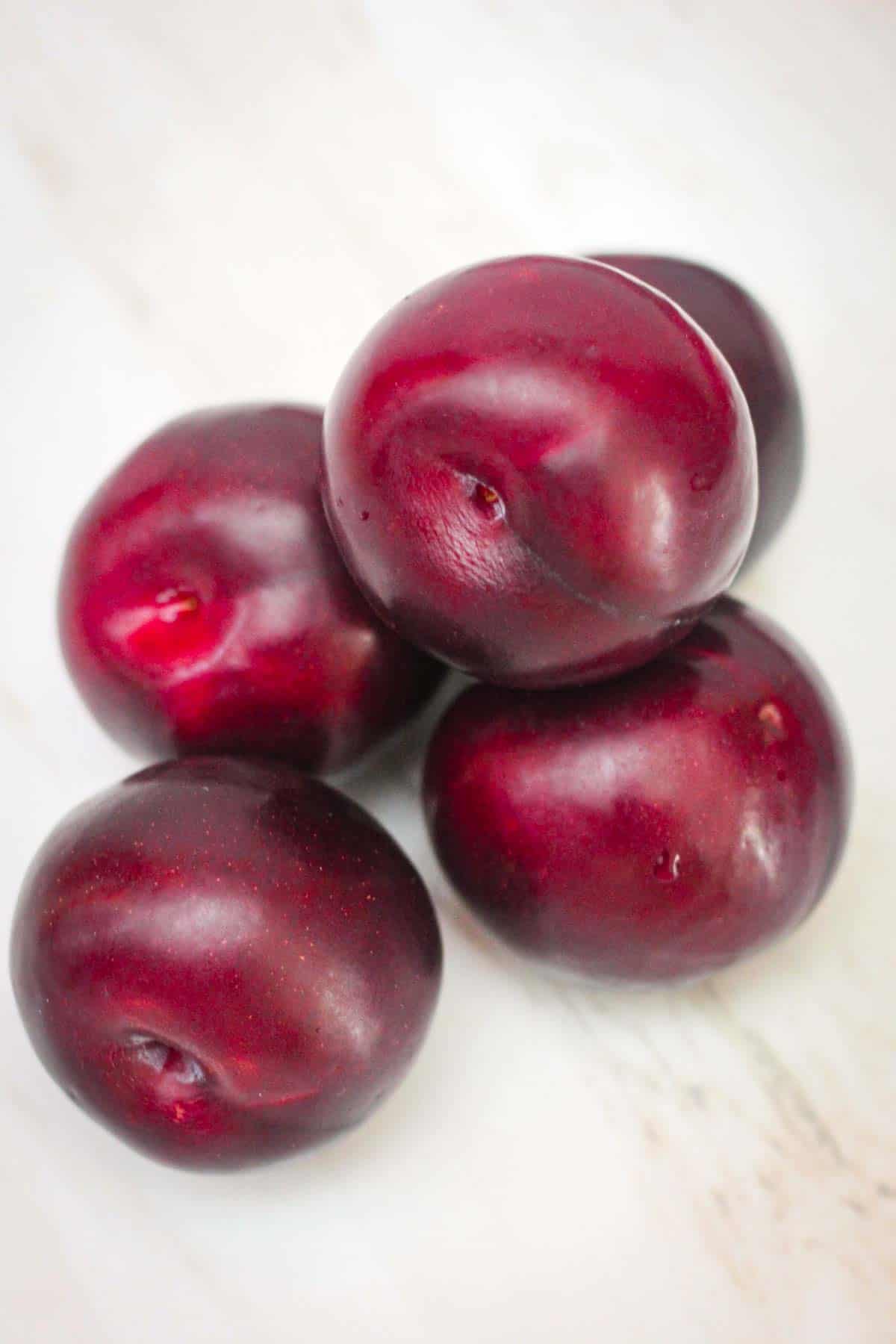 About 5 plums next to each other, on a counter.