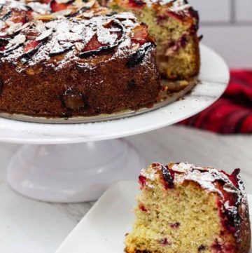 Plum Almond cake on a cake stand and a slice of the cake on a plate in the forefront.