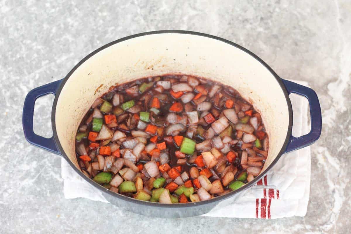 The cooked veggies in Dutch oven are covered in red wine. 