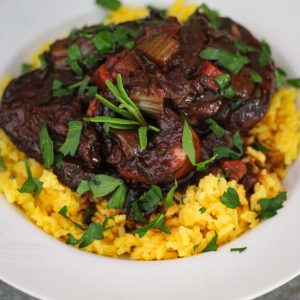 Braised beef shanks served over yellow rice and garnished with fresh herbs.