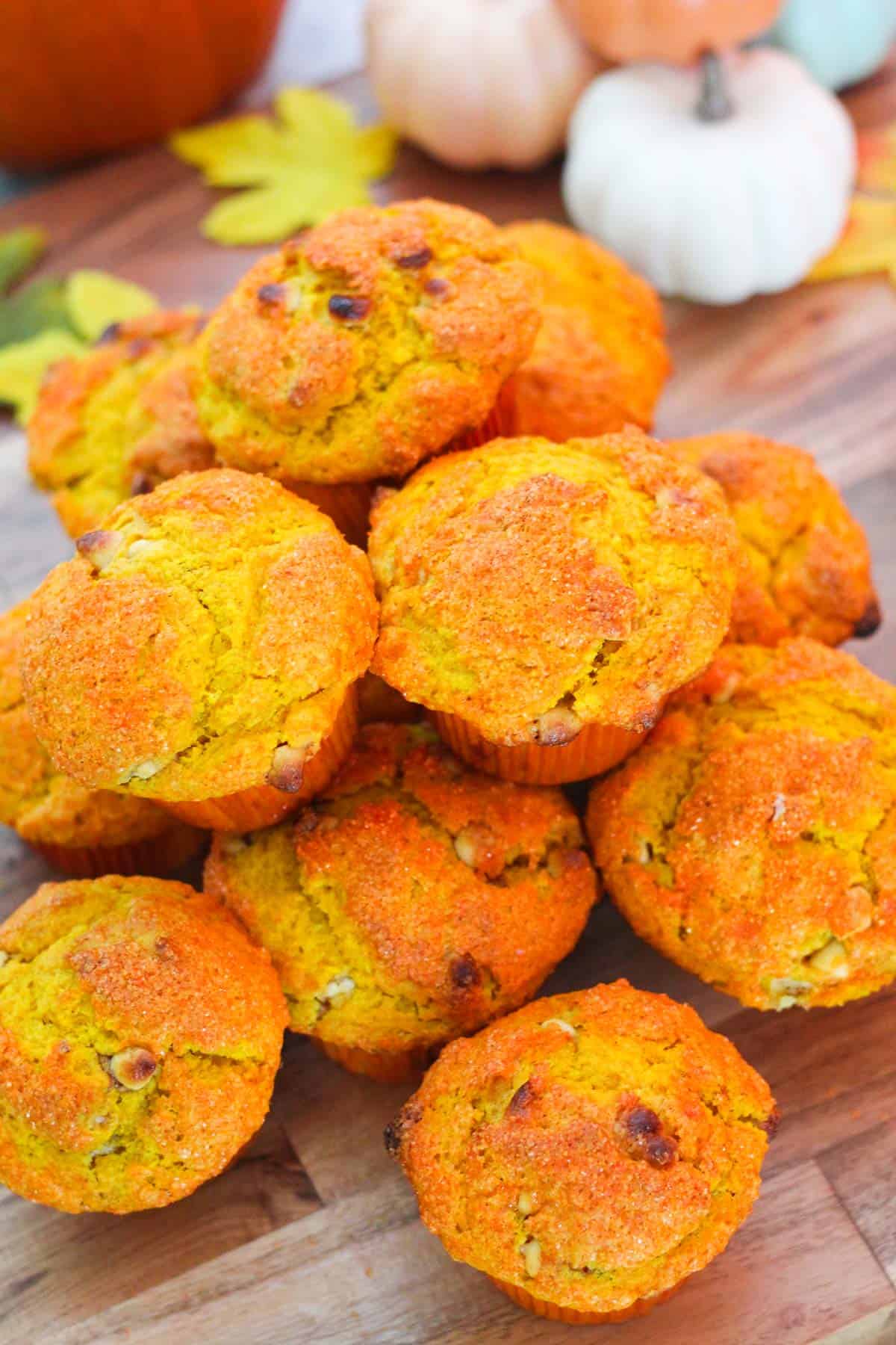 Bright orange muffins, they're pumpkin muffins with white chocolate chips on top of each other in a board.