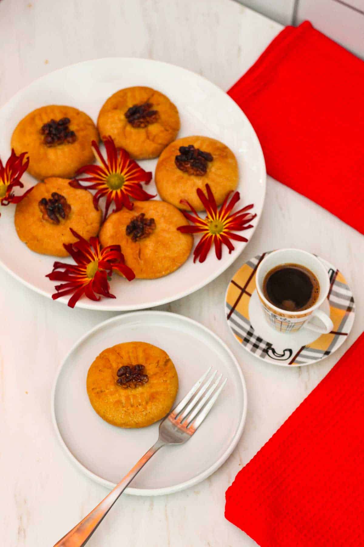 A plate with sheqerpare cookies garnished with flowers. Then there's a serving plate with one of the cookies and fork in it. We can also see a small coffee on the right hand side.