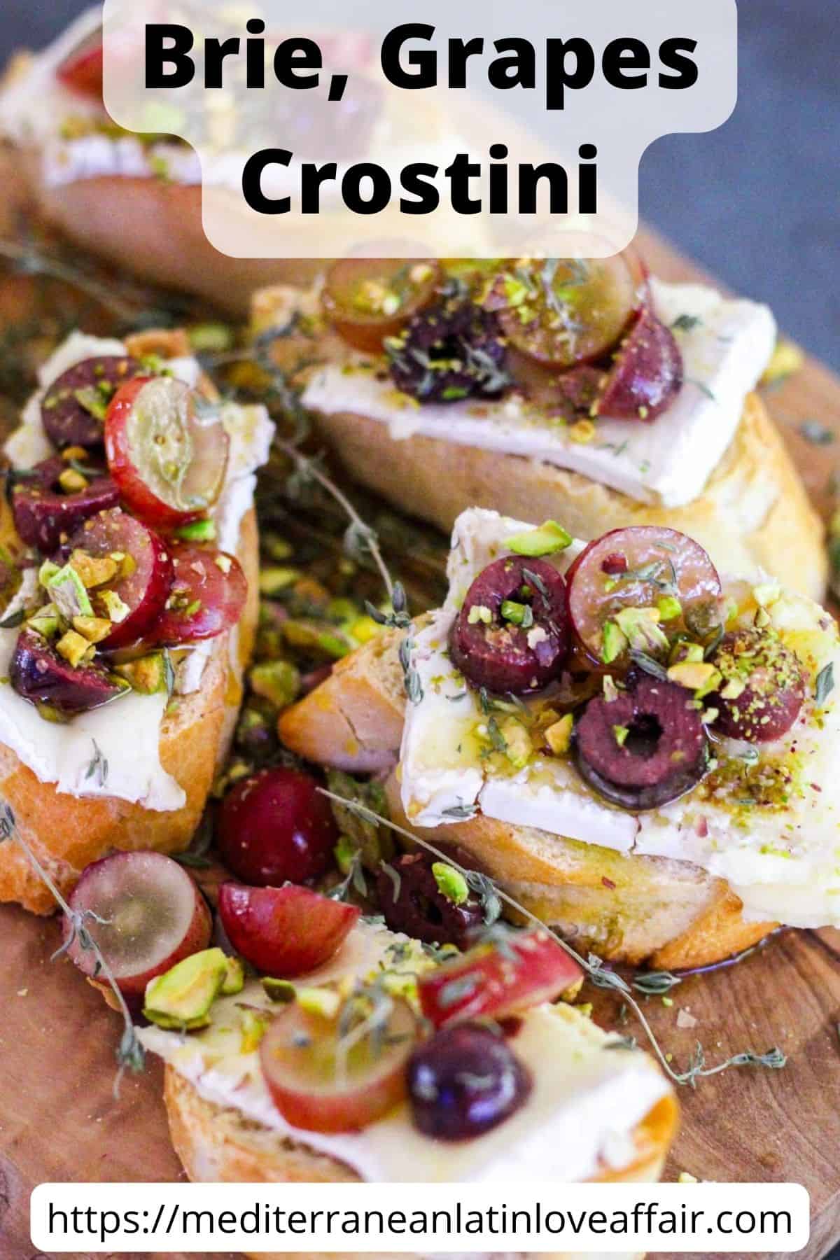 An image prepared for Pinterest. It shows brie, grapes crostini with olive and pistachios on a cheese board. The image has a title bar on top and a website link at the bottom.
