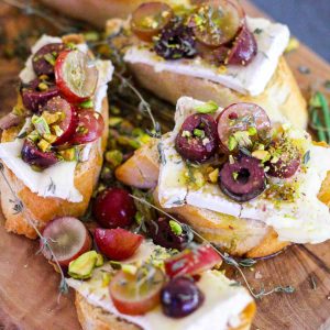 Crostinis made with baguette and topped with brie cheese, slices grapes, olives and pistachios.