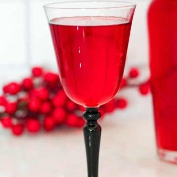 An image created for Pinterest. It shows a picture of a glass and a bottle of the freshly made cranberry liqueur. There's a title bar on top of the picture and a website link at the bottom.
