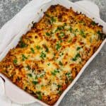 A casserole dish with baked pasta and cheese shown from above. There's a kitchen towel next to the dish and the dish itself is garnished with fresh parsley.