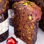 Pistachio chocotone sliced in half and picture shows the inside of one of the slices. There's a partial uncut panettone on the side and Christmas decor around them.