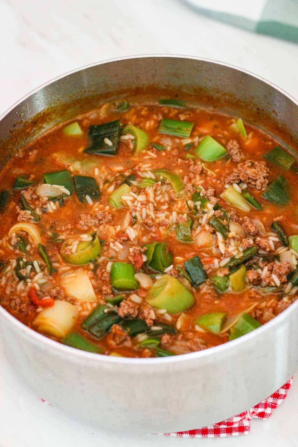 Pot with cooked leeks, rice, tomatoes and other ingredients.