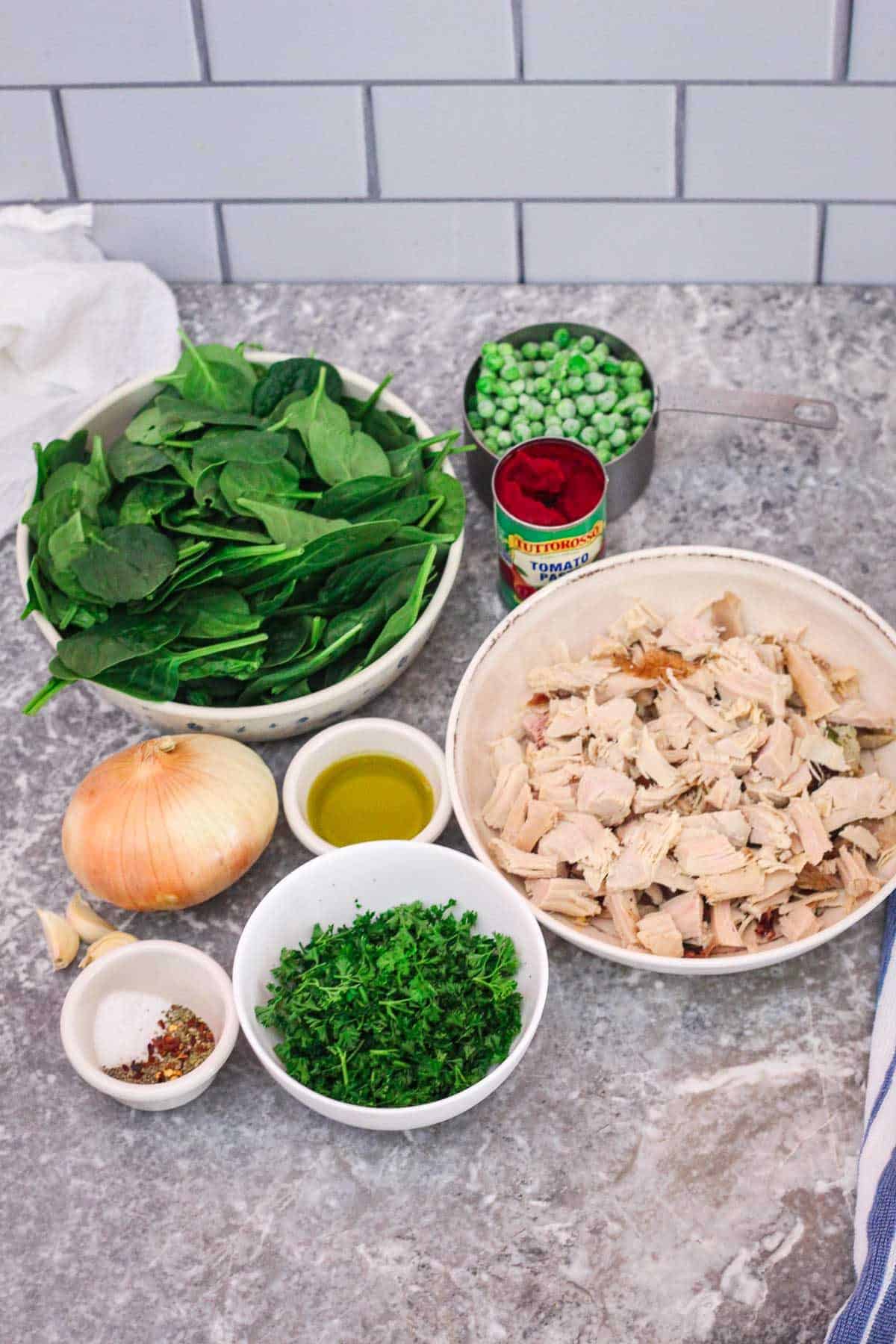 Some of the ingredients shown next to each other: spinach, tomato paste, green peas, onion, olive oil, turkey meat, garlic, fresh parsley and a little container with salt, spices and herbs.