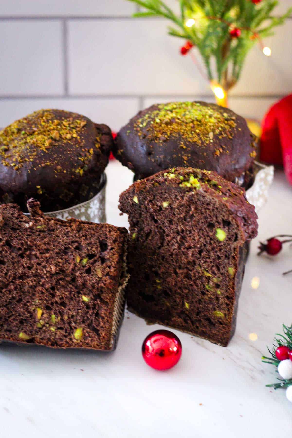 Baked mini panettones with chocolate and pistachios. One is panettone is front and center and cut in half so you can see the inside.