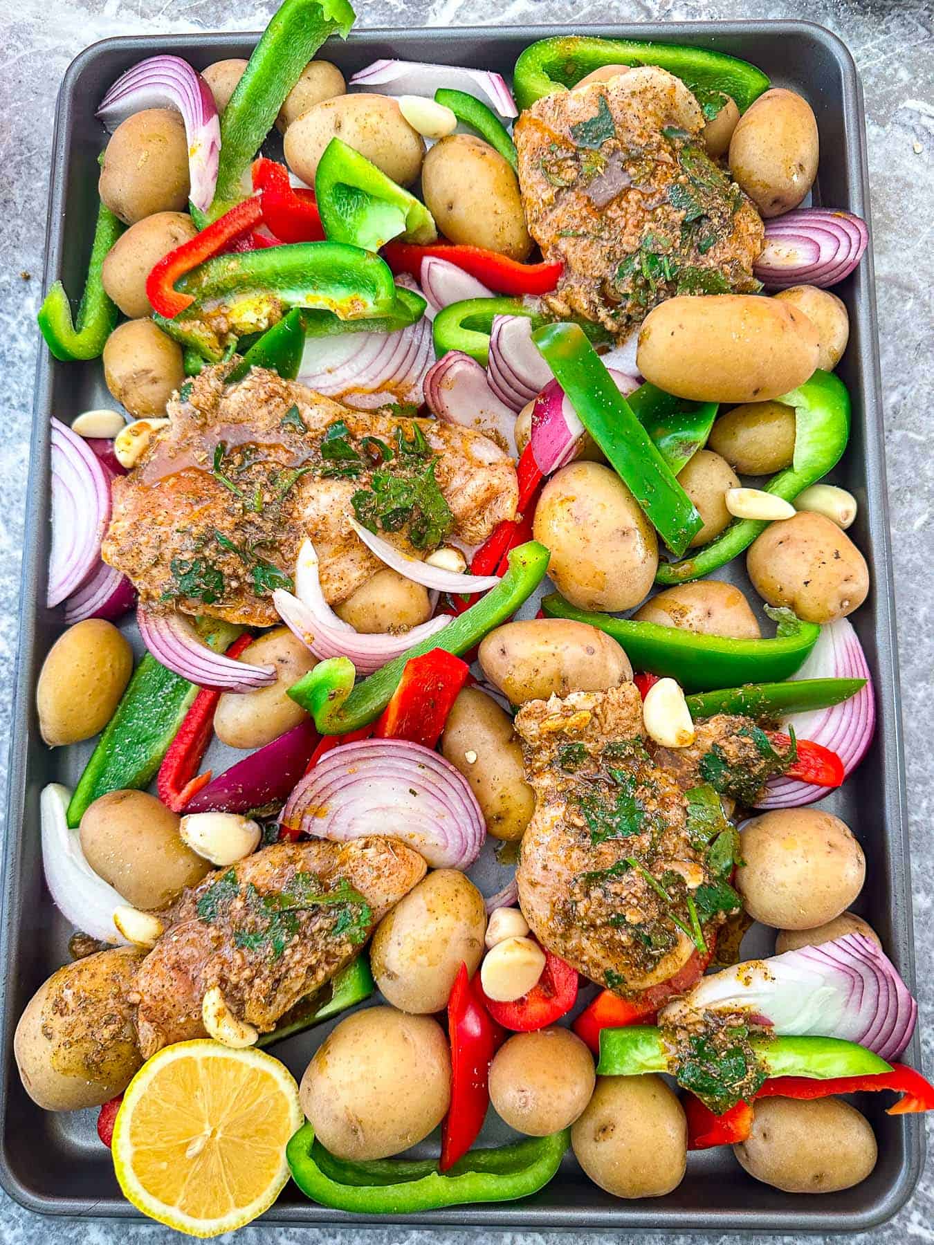 Sheet pan with chicken and veggies like potatoes, bell peppers, onions etc ready to bake.