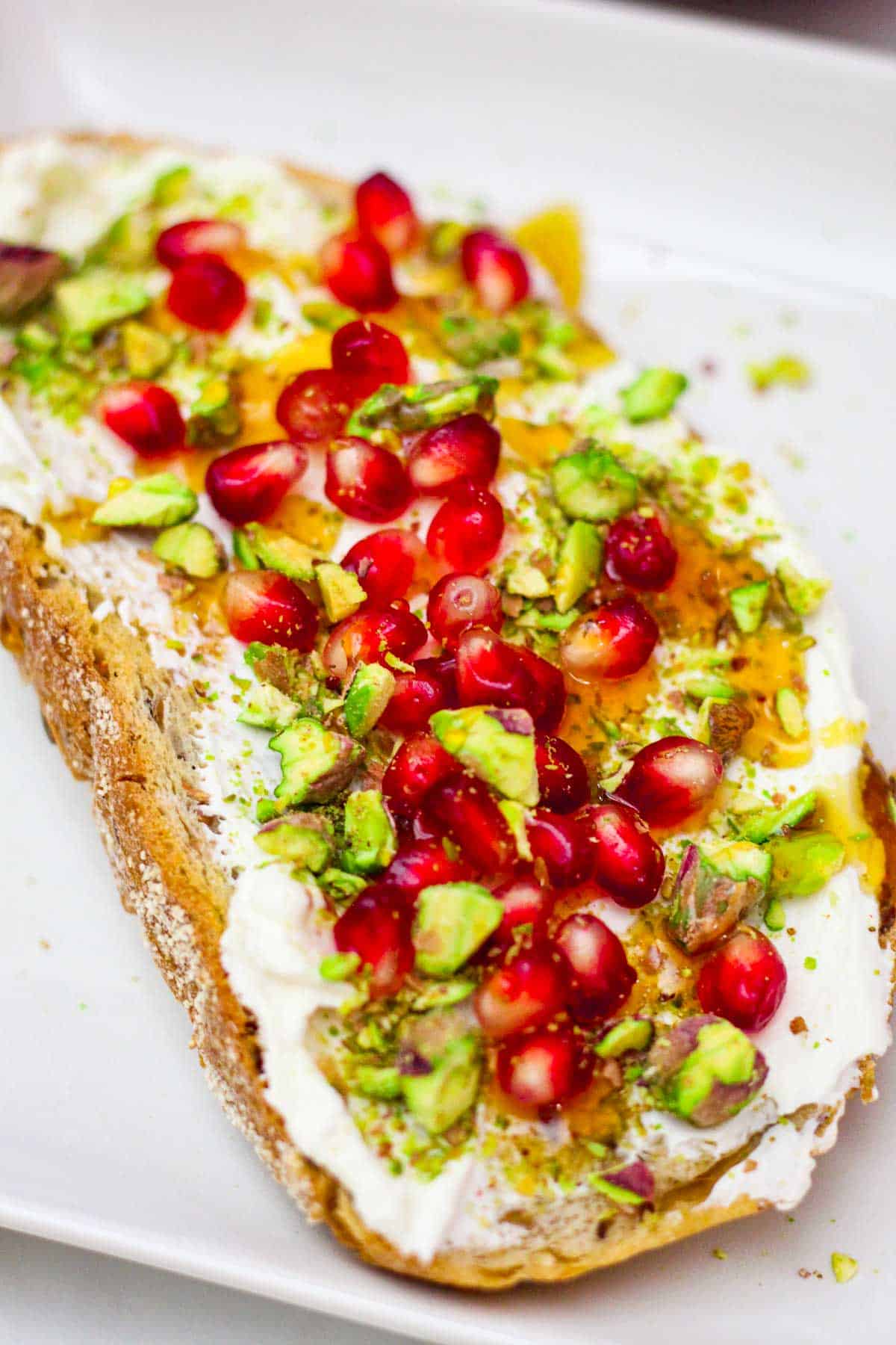 Strained yogurt spread over sourdough bread with pomegranate, pistachios and honey.