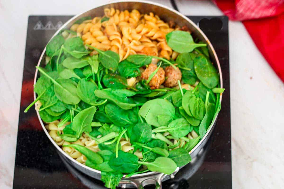 Adding pasta, sausages and spinach to sauce in the pan.