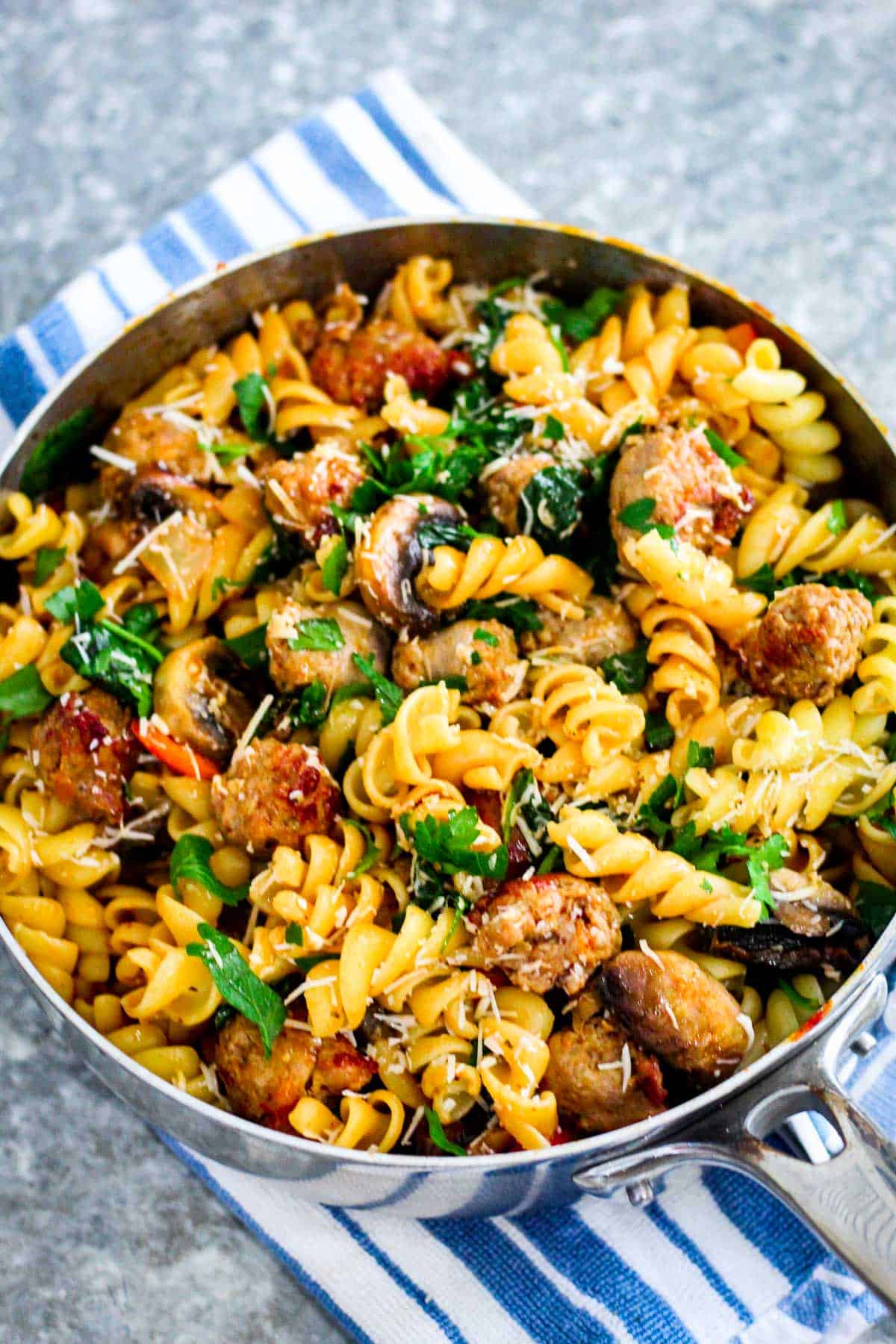 Fusilli pasta with sausages, spinach, mushrooms and cheese shown in a deep pan, ready to serve family style.