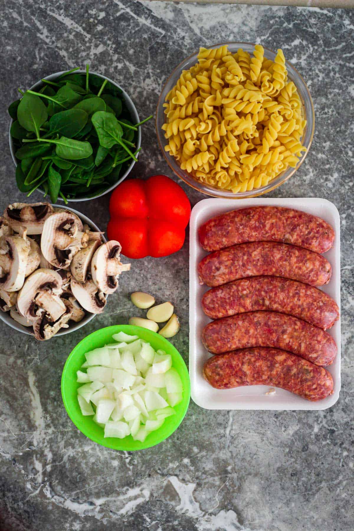 Ingredients for Fusilli pasta with sausages dinner - spinach, fusilli, red bell pepper, mushrooms, garlic, sausages, onion.