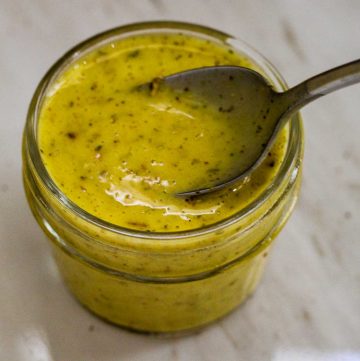 A small mason jar with Meyer lemon vinaigrette, shown with a spoon in it.