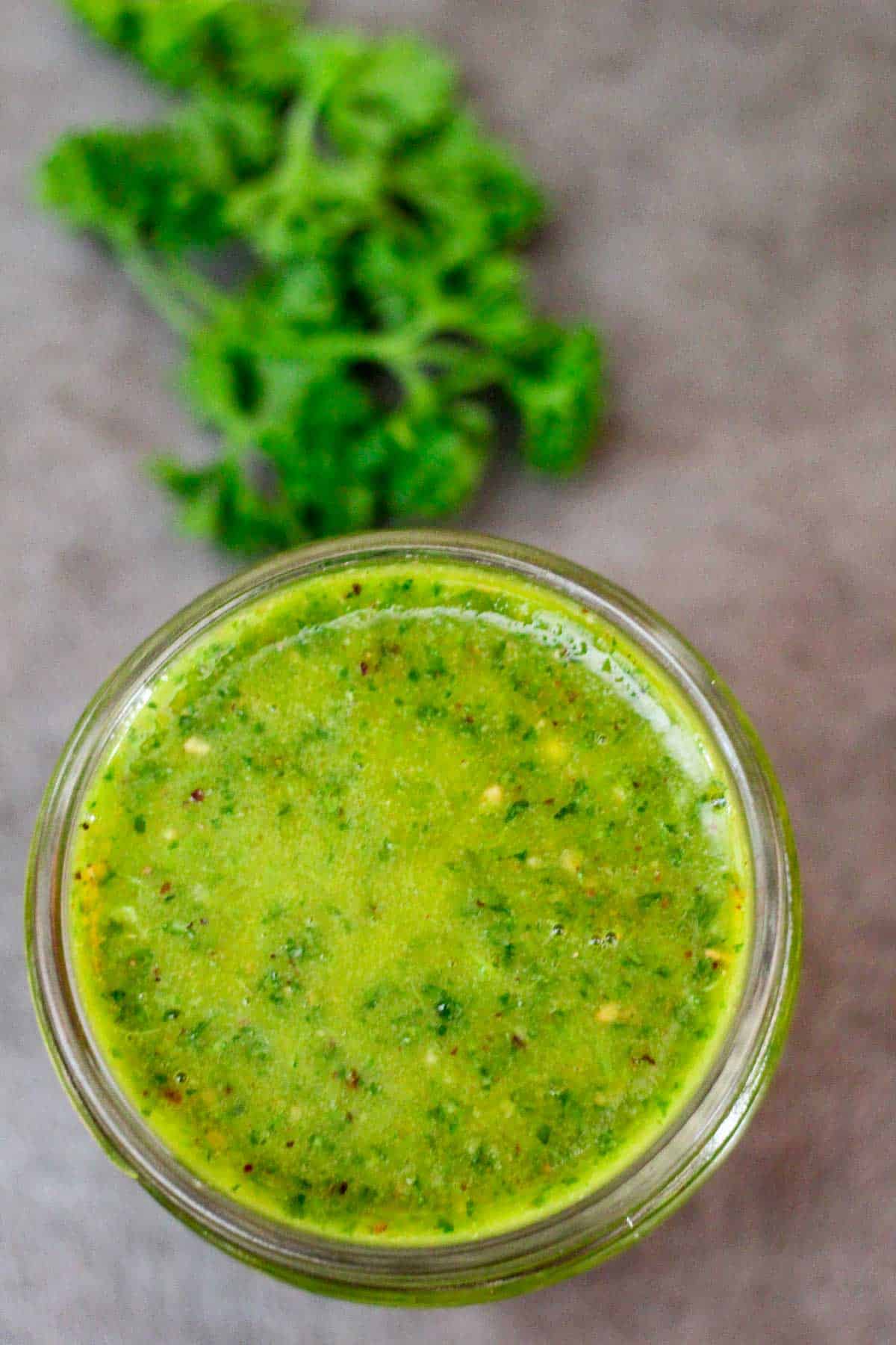Parsley za'atar sauce or marinade on a jar. You can see some fresh parsley next to the jar.