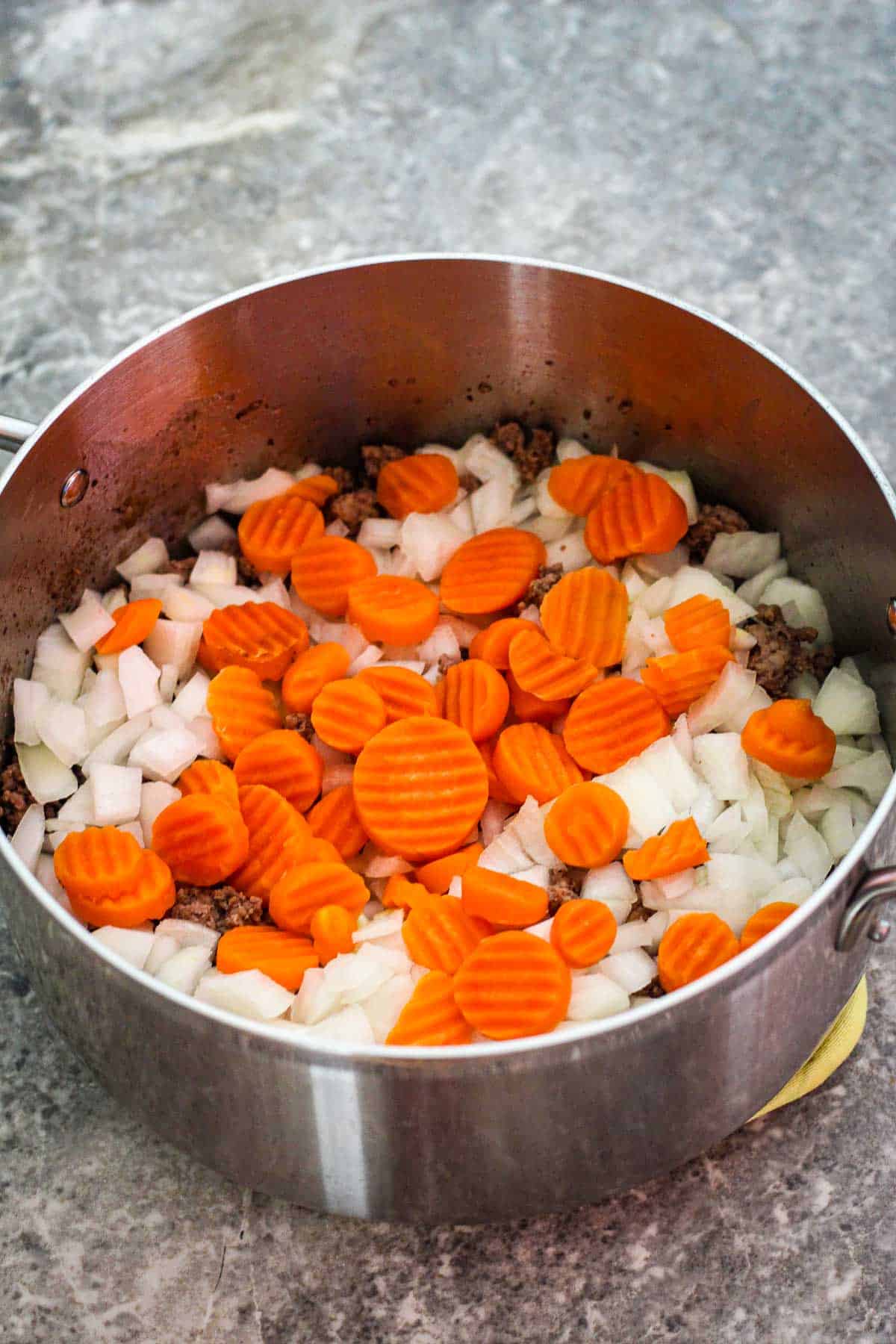 Adding chopped onions and carrots to pot over browned meat.