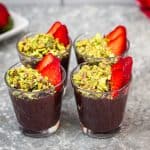 Four glass cups with chocolate pudding, topped with crushed pistachios and sliced strawberries.