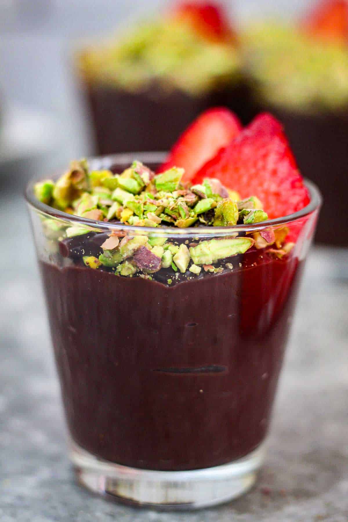Center of the picture you see a glass with chocolate pudding topped with pistachios and strawberries. There are similar cups (though blurred) in the background.