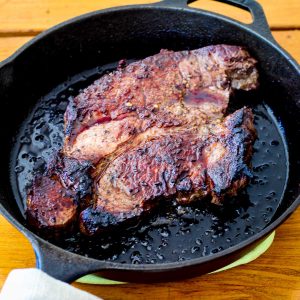 A cast iron skillet over a table, showing a just cooked huge chuck steak.