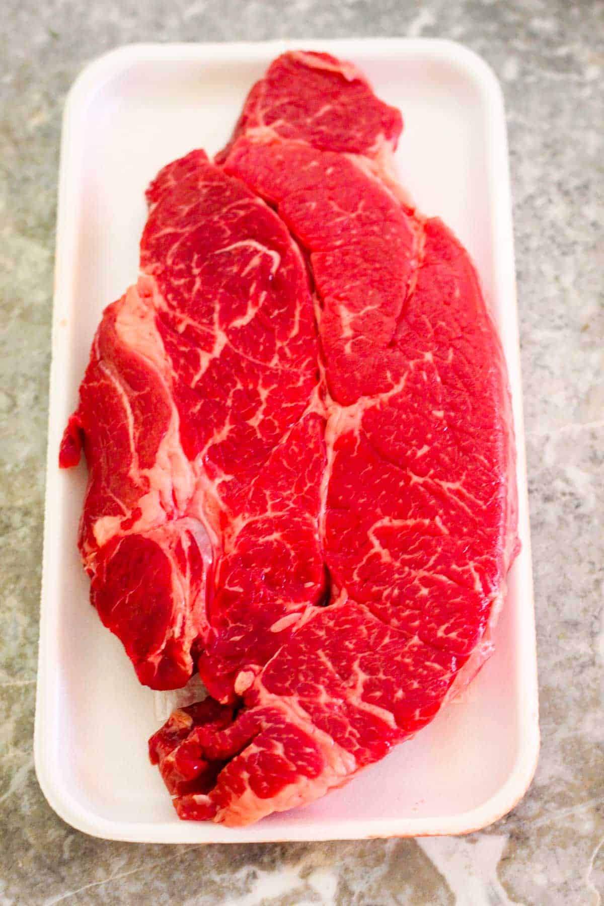 Raw Chuck steak still on store package over a counter.