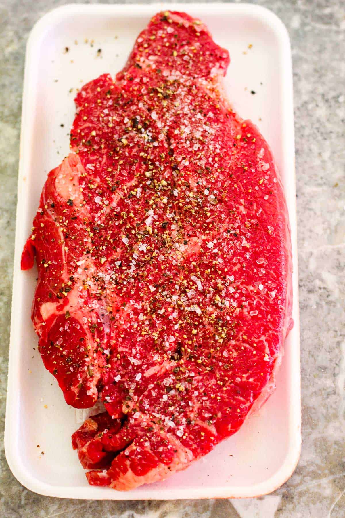 Chuck steak in package, now seasoned with coarse sea salt and pepper. Steak is still raw.
