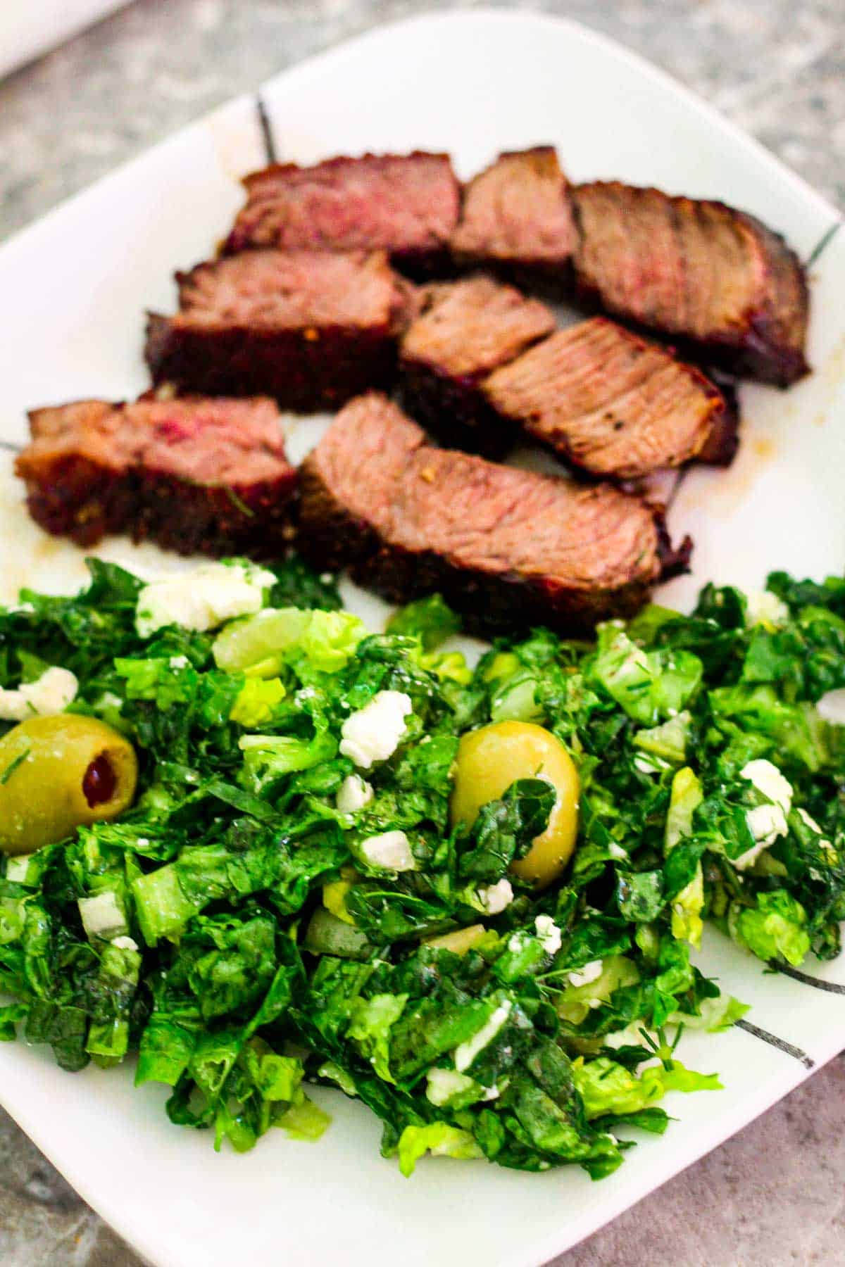 A serving of sliced chuck steak with lettuce dill salad and feta cheese. 