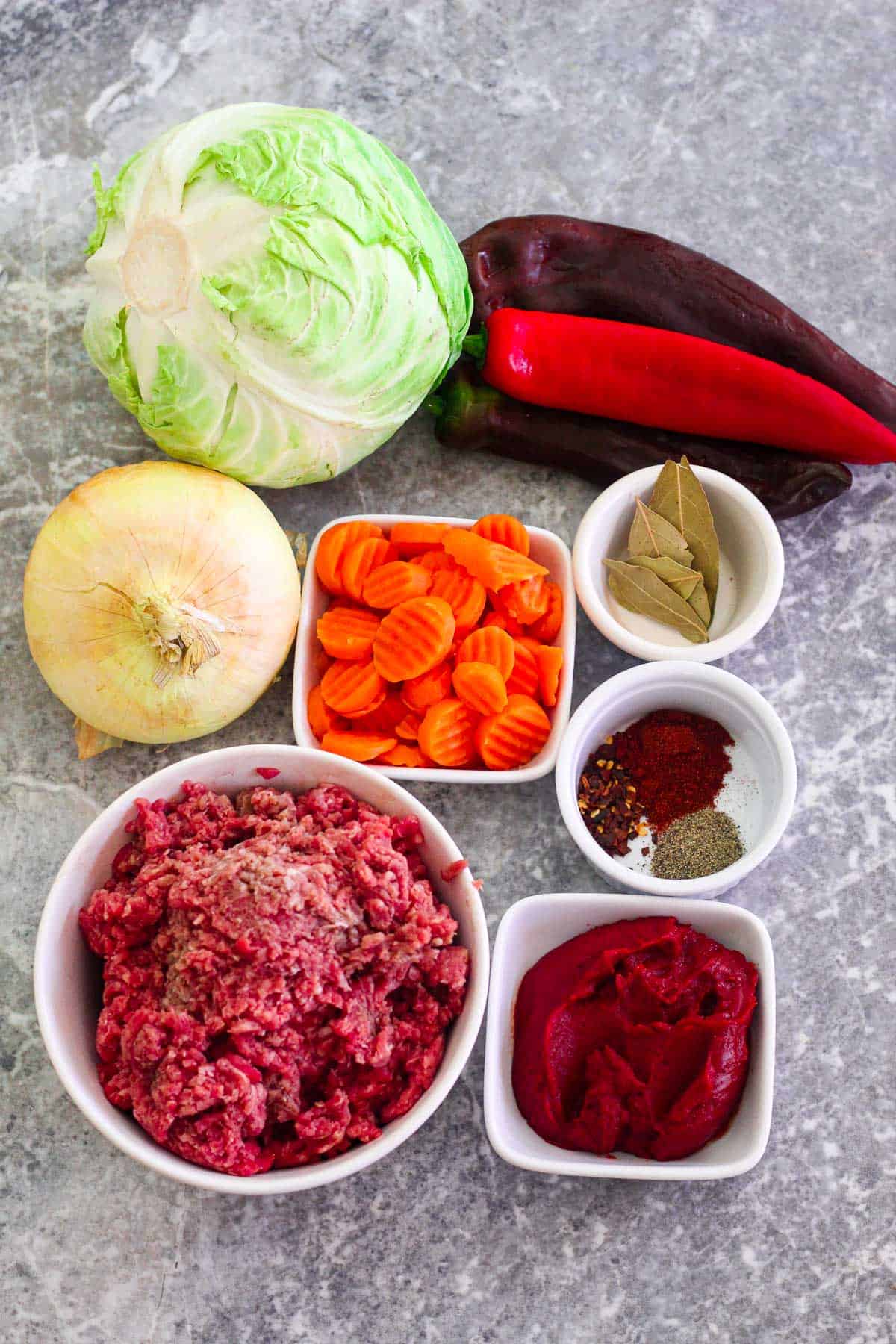 Ingredients for braised cabbage with ground beef: cabbage, peppers, onion, carrots, bay leaves, ground beef, paprika, black pepper, crushed red pepper, tomato paste.