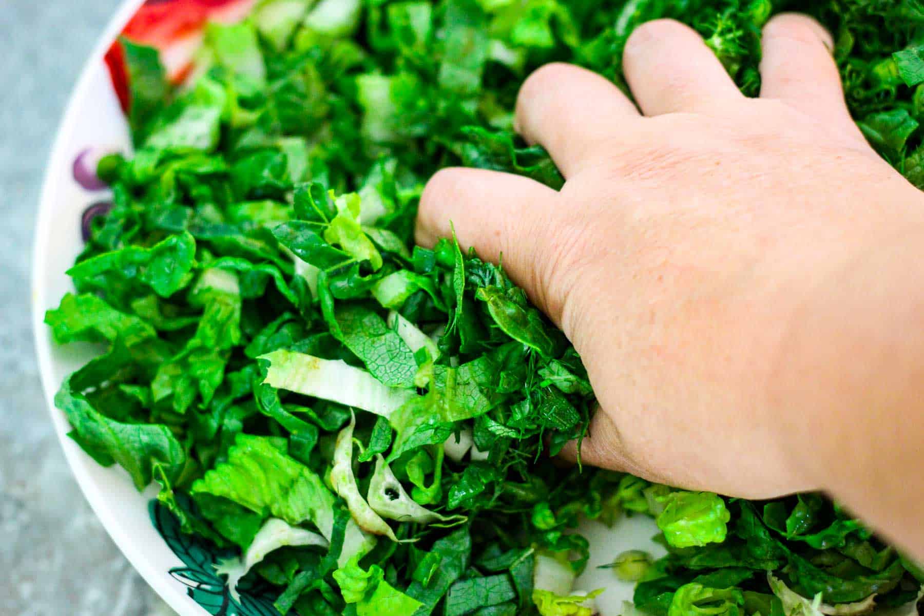 Massaging lettuce, dill, scallions and salt and lemon to fuse flavors. Picture shows a hand over the salad bowl squeezing all the ingredients together. 