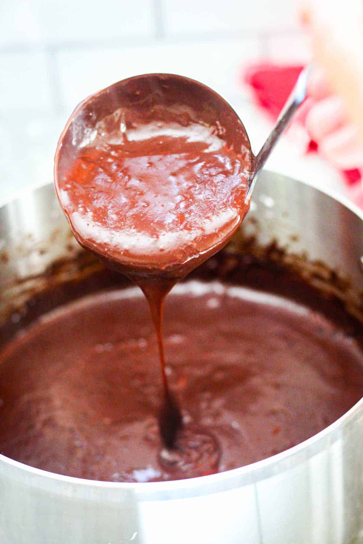 Chocolate pudding in the sauce pan, ready to pour into serving cups. Picture shows a ladle pouring the chocolate pudding back into the saucepan, almost like dripping from ladle just to show consistency of pudding.