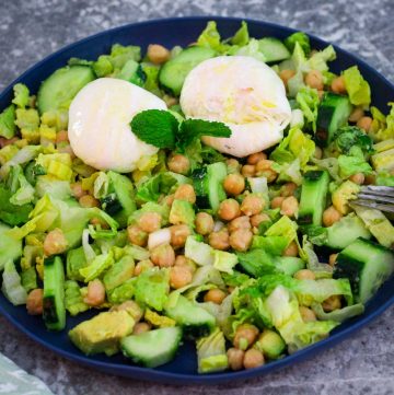 Chickpea and Cucumber salad on a blue plate garnished with mint. You can also see lettuce and avocados peaking through in the salad:).