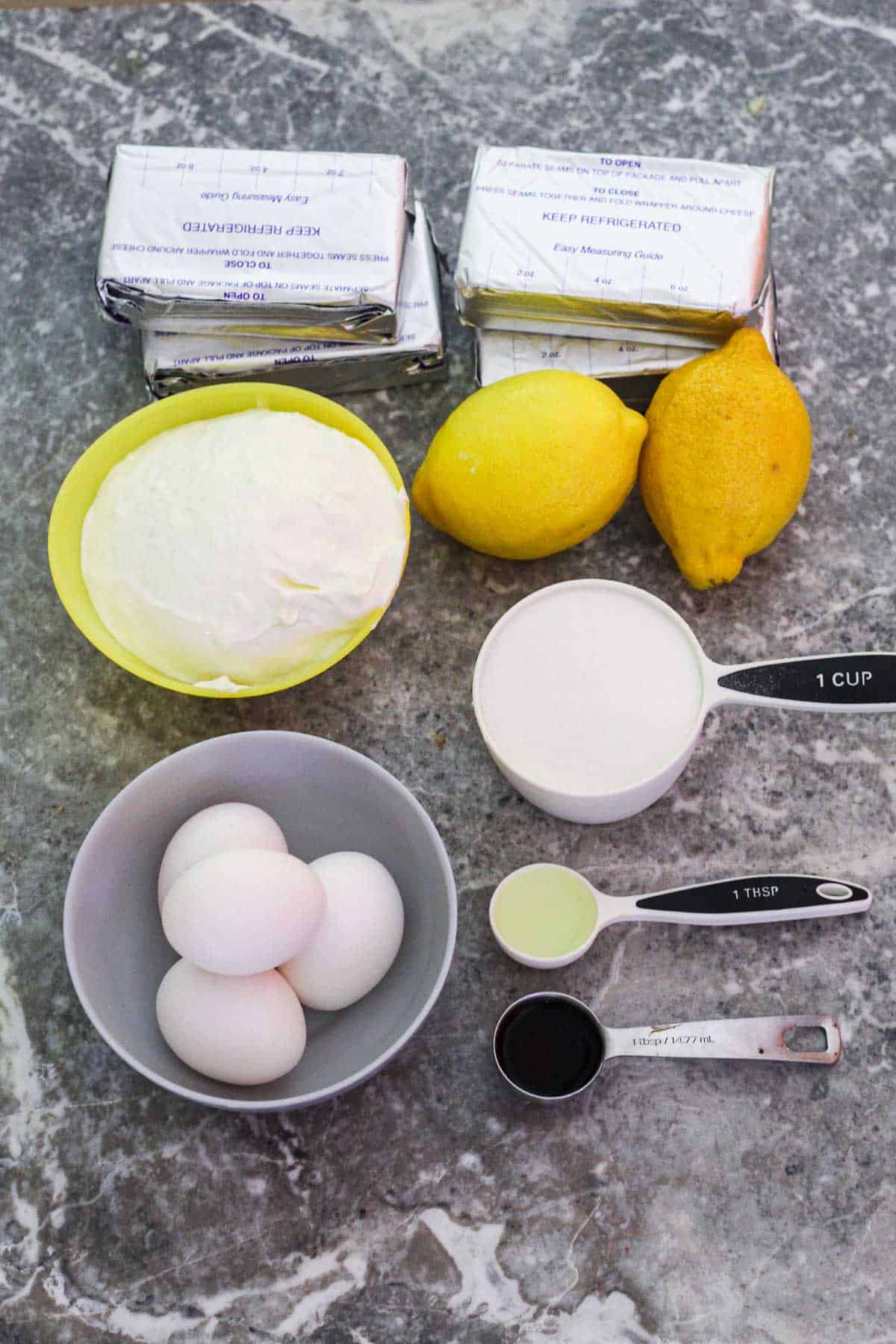 Ingredients for lemon cheesecake filling: cream cheese, lemons, sour cream, eggs, vanilla extract, lemon extract, sugar.