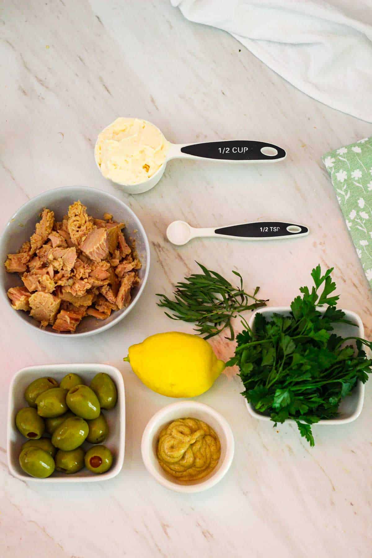 Ingredients for tuna dip: tuna in a bowl, mayonnaise, salt, tarragon, lemon, parsley, green olives and mustard.