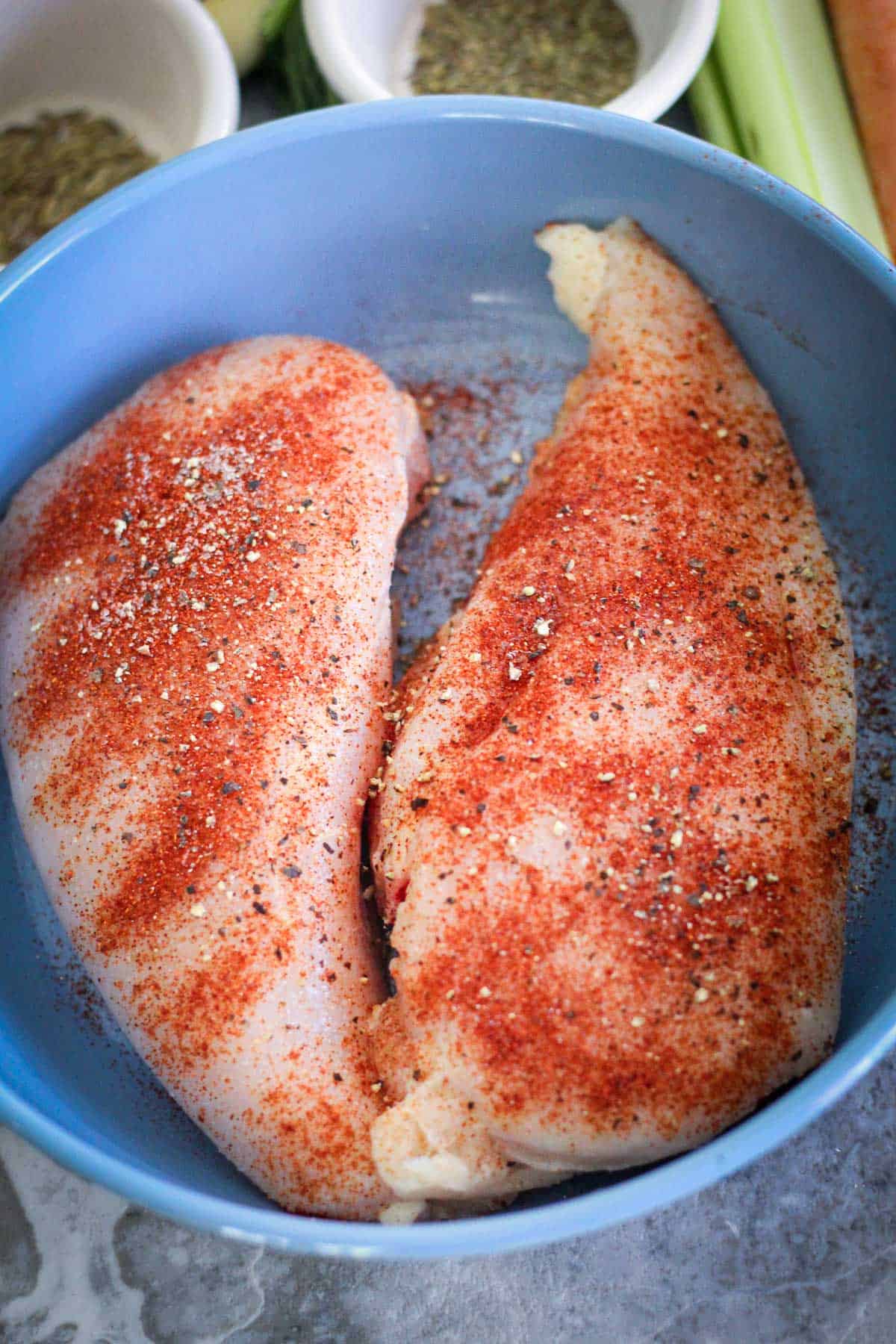 Two seasoned chicken breasts on a plate. Seasoning has salt, pepper and paprika.