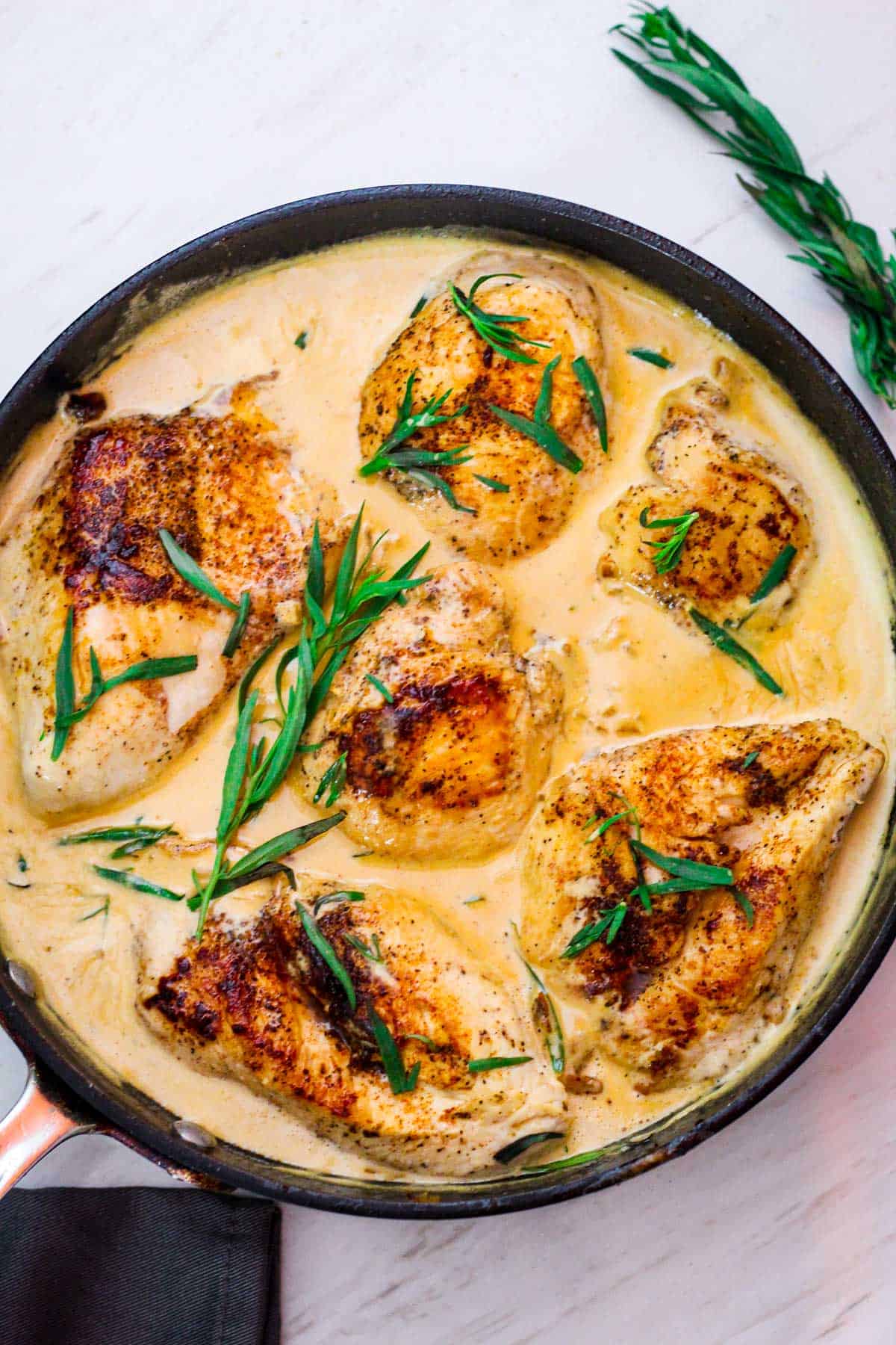 Tarragon chicken in white wine sauce, shown in a skillet already cooked and garnished with tarragon.