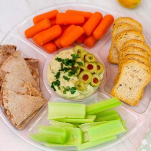 Tarragon tuna dip with olives, parsley and lemon on a appetizer tray with compartments. Tuna dip is in the middle, surrounded by pita bread, carrots, toasts, celery etc.