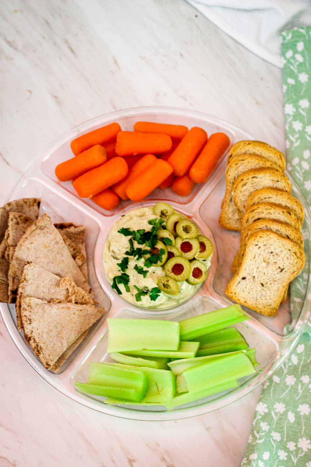 Tuna dip with tarragon served with carrots, celery, pita bread and crostini while garnished with parsley and olive slices. 