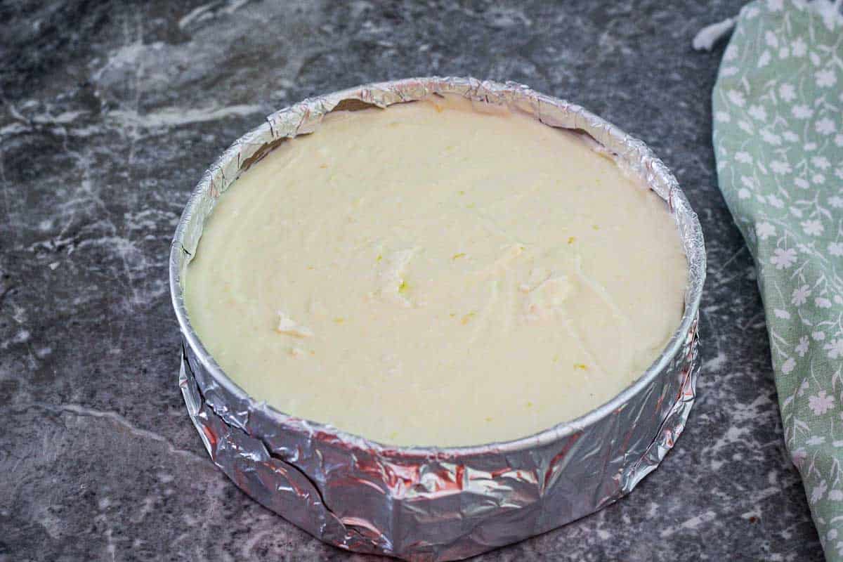 Cheesecake ready to bake in a springform pan wrapped in aluminum foil. 