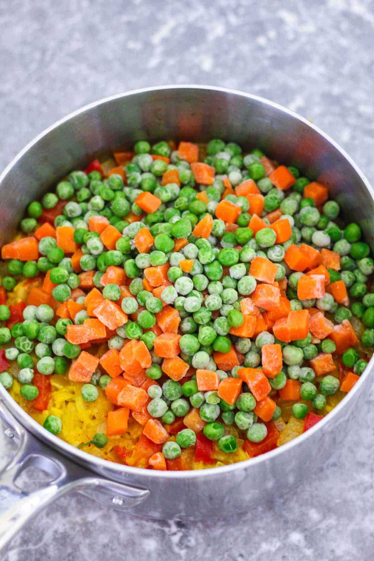 Adding frozen peas and carrots to rice.
