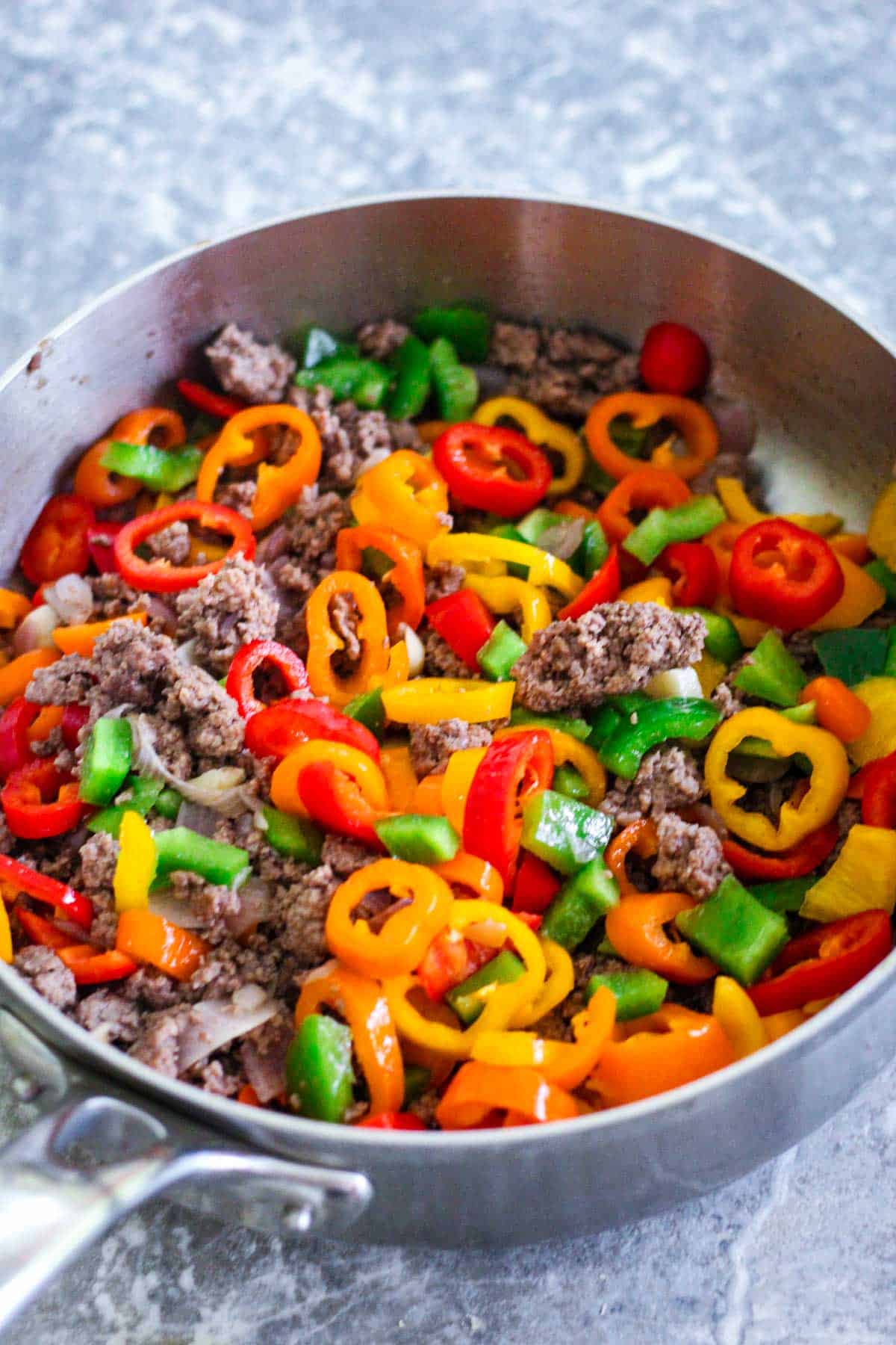Adding chopped peppers over browned beef.