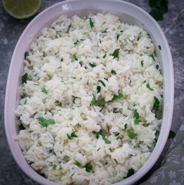 A ceramic, oval bowl containing cilantro lime rice with garnishes around the bowl.